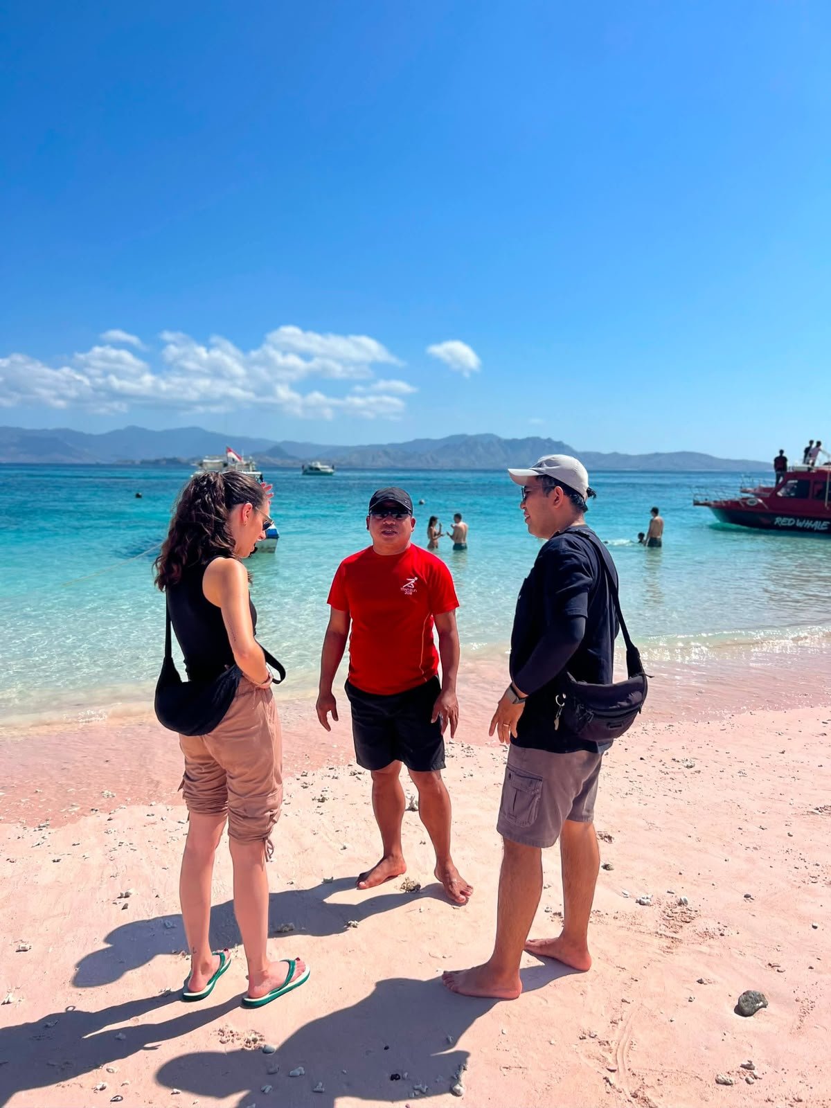 Three people standing on the pink sand shoreline of Pink Beach in Komodo National Park