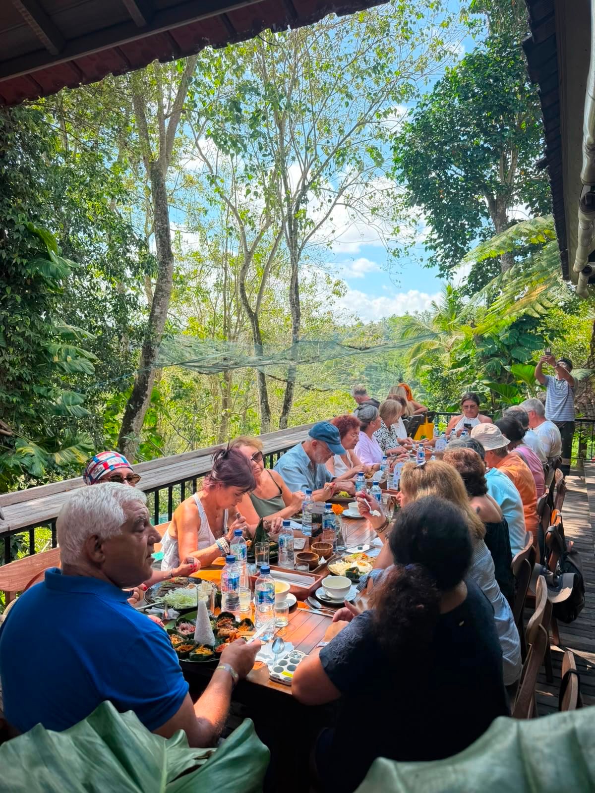 The group at a long table on an open deck at d'Alas Restaurant near Ubud, overlooking a forested river valley
