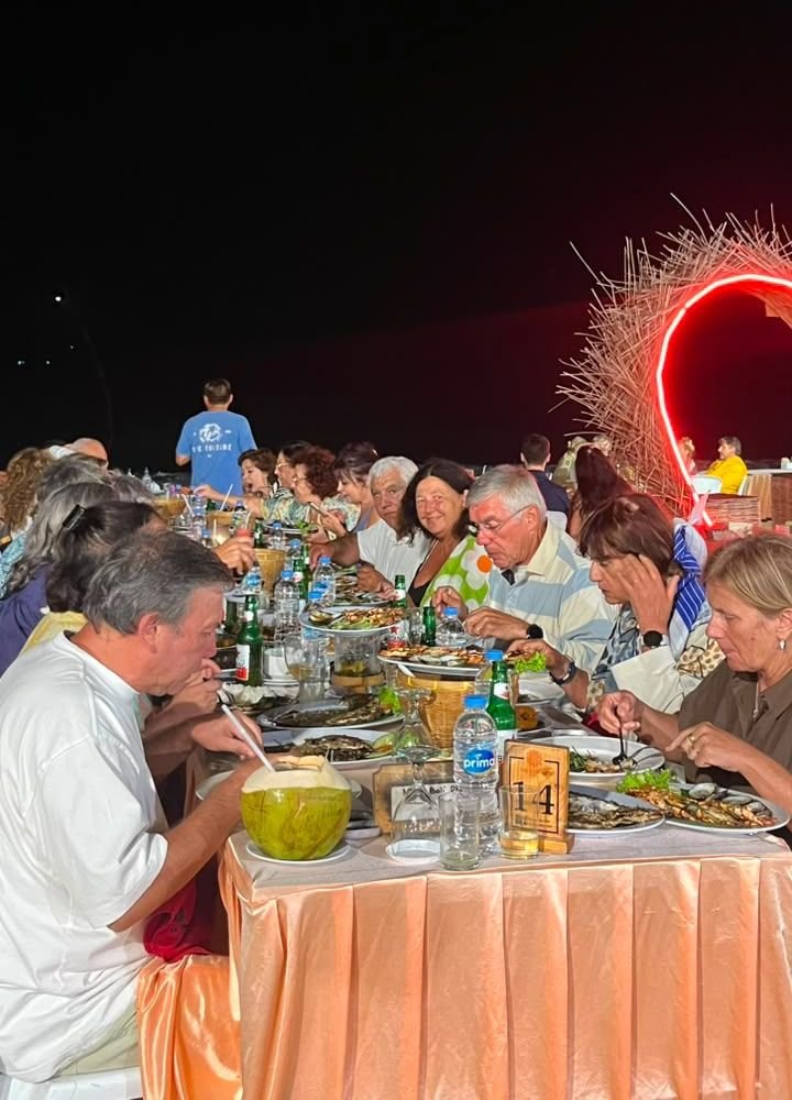 The group seated at a long beachfront table for a grilled seafood dinner at night in Kedonganan, Bali