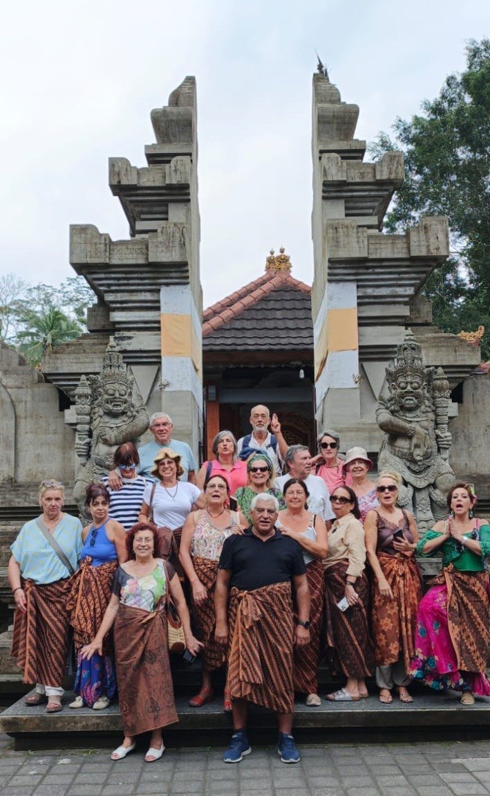 The Portuguese group wearing traditional Balinese sarongs at a split temple gate flanked by stone guardian statues